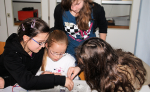 Ältere Schülerinnen zeigen einer jüngeren Schülerin ein naturwissenschaftliches Experiment.